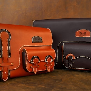 Puede incluir: Dos bolsos de cuero en un esquema de color marr&oacute;n y naranja. El bolso m&aacute;s grande tiene una solapa con una correa de cuero marr&oacute;n y una hebilla. El bolso m&aacute;s peque&ntilde;o tiene una solapa con una correa de cuero marr&oacute;n y una hebilla. Ambos bolsos tienen un bolsillo en la parte delantera. El bolso m&aacute;s grande tiene el texto "CREATIVE AWLS" en la parte delantera.