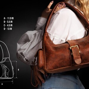 Puede incluir: Un bolso de hombro de cuero marr&oacute;n con cierre de hebilla y un peque&ntilde;o bolsillo lateral. El bolso mide 30 cm de ancho, 14 cm de alto y 33 cm de profundidad.