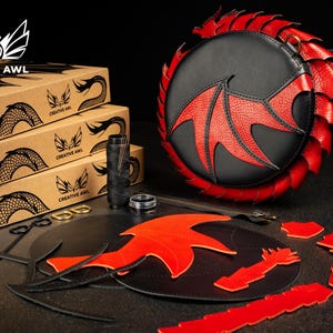 May include: A black and red dragon-themed leather bag with matching craft supplies. The bag features a dragon wing design and a red scale trim. The image also shows boxes with the Creative Awl logo.