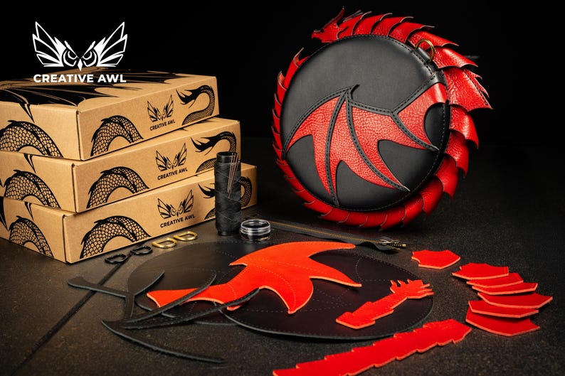 May include: A black and red dragon-themed leather bag with matching craft supplies. The bag features a dragon wing design and a red scale trim. The image also shows boxes with the Creative Awl logo.