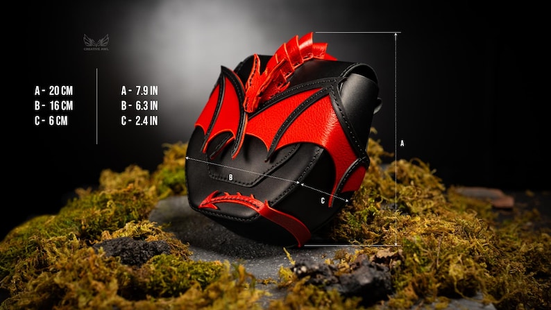 Op de afbeelding: Een zwarte en rode tas met draakthema, voorzien van een gebeeldhouwde drakenkop en vleugels op de voorflap. De afmetingen zijn aangegeven als A: 20 cm, B: 16 cm en C: 6 cm. De tas heeft een textuurafwerking en een puntig staartdetail onderaan.