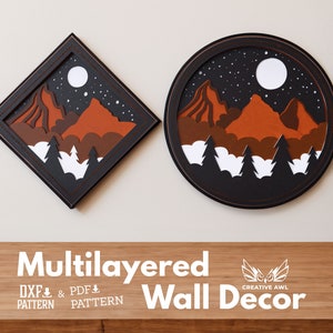 Puede incluir: Dos piezas de decoración de pared de papel en capas, una cuadrada y otra redonda, ambas representando una escena de montaña con una luna y estrellas en el cielo nocturno. El texto "Multilayered Wall Decor" está debajo de las piezas.