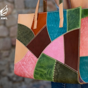 May include: A rectangular tote bag constructed from multi-coloured leather patches in shades of pink, green, blue, brown, and tan. The panels are joined with visible white cross-stitching. It features two light tan leather handles at the top.