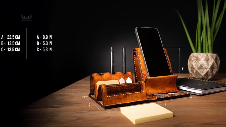 May include: A brown leather desk organizer with a phone holder, pen holders, and a notepad section. The organizer is 8.9 inches wide, 5.3 inches high, and 5.3 inches deep. Two pens are in the pen holders.
