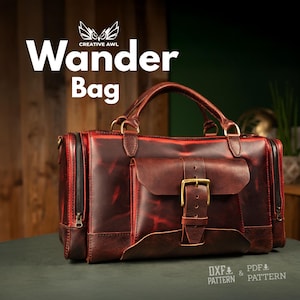 May include: A handcrafted, reddish-brown leather Wander Bag with a top handle, side zippers, and a front flap secured by a brass buckle. The bag features the text "Wander Bag" and the Creative AWL logo.