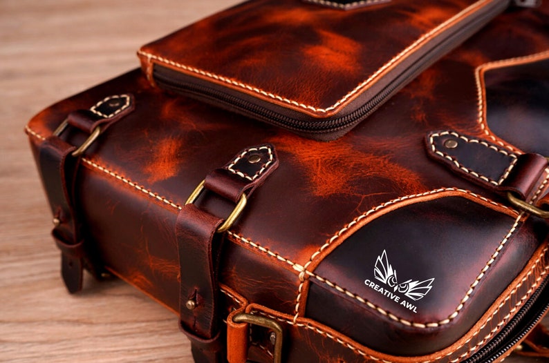May include: A brown leather backpack with a front pocket and a logo that says "Creative Awl". The backpack has a distressed look and is made of high-quality leather.