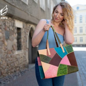 May include: A rectangular tote bag constructed from multi-coloured leather patches in shades of teal, dark brown, olive green, light pink, and beige. The bag features visible stitching along the seams and two light tan leather shoulder straps.