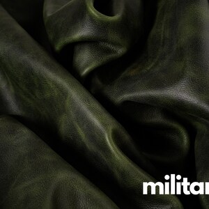 May include: Close-up of a dark green leather fabric with a textured surface. The fabric is folded and draped, showing the natural grain and folds of the leather.