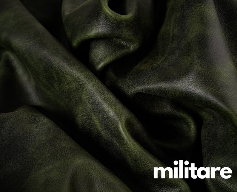 May include: Close-up of a dark green leather fabric with a textured surface. The fabric is folded and draped, showing the natural grain and folds of the leather.