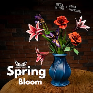 Puede incluir: Un jarrón azul contiene un vibrante arreglo floral de flores de papel, que incluye rosas rojas, lirios rosas e iris moradas. El arreglo está sobre una mesa de madera. Las palabras "Spring Bloom" se muestran en texto blanco.