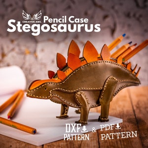 May include: A brown leather pencil case shaped like a Stegosaurus dinosaur. The case has orange plates on its back and a zipper opening. The text "Pencil Case Stegosaurus" is above the case. The text "DXF PATTERN & PDF PATTERN" is below the case.