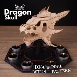 May include: A beige dragon skull sculpture with detailed features, mounted on a black, hexagonal base. The base has red stitching and holds several lit tealight candles. The image includes the text "Dragon Skull" and "DXF & PDF PATTERN".
