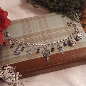 May include: A silver charm bracelet with various charms, including a rose, a teacup, a mirror, and a wolf. The charms are attached to a silver chain bracelet.