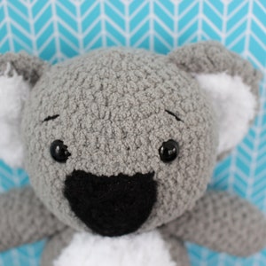 Peut inclure: Un jouet en peluche koala gris crocheté avec des yeux noirs, un nez noir et de la fourrure blanche sur les oreilles.