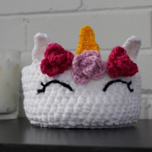 Peut inclure: Tête de licorne blanche en crochet avec des accents de fleurs roses et rouges et une corne jaune.