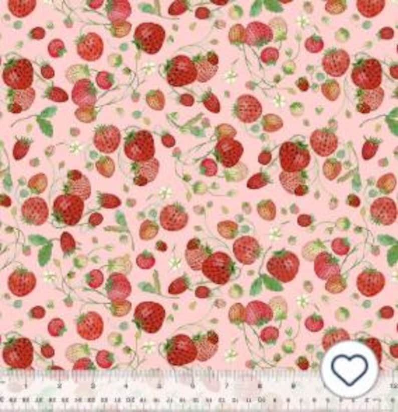May include: A fabric with a repeating pattern of red strawberries, green leaves, and white flowers on a light pink background. The strawberries vary in size and are scattered across the fabric. A ruler is at the bottom.