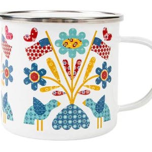May include: White enamel mug with a silver rim and a white handle. The mug is decorated with colorful floral and bird designs, along with red, white, and blue flag and heart motifs. The mug is approximately 3.5 inches tall.