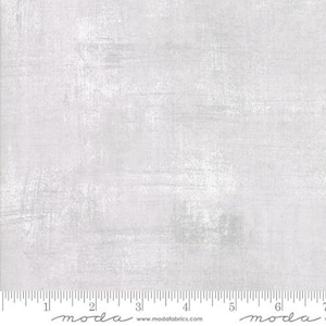 May include: A light gray fabric with a subtle textured pattern. The fabric has a slightly distressed look, with a hint of white throughout. The fabric is perfect for quilting, sewing, and crafting.
