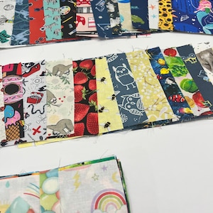 May include: A collection of colorful fabric squares with various patterns, including animals, food, and geometric designs. The squares are arranged in rows and columns, creating a patchwork effect.