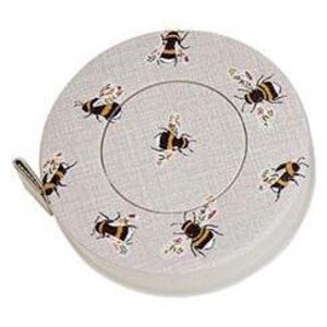 May include: A round, light gray measuring tape with a bee pattern. The tape measure has a white and black bee design with floral accents. The tape measure is in a circular case with a small fabric pull tab.
