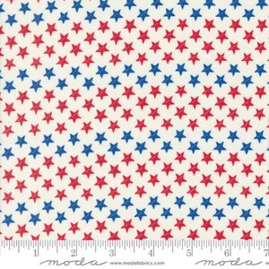 May include: Cream-colored fabric with a repeating pattern of red and blue stars. The stars are evenly spaced and arranged in rows. A ruler is at the bottom of the fabric, with measurements in inches.