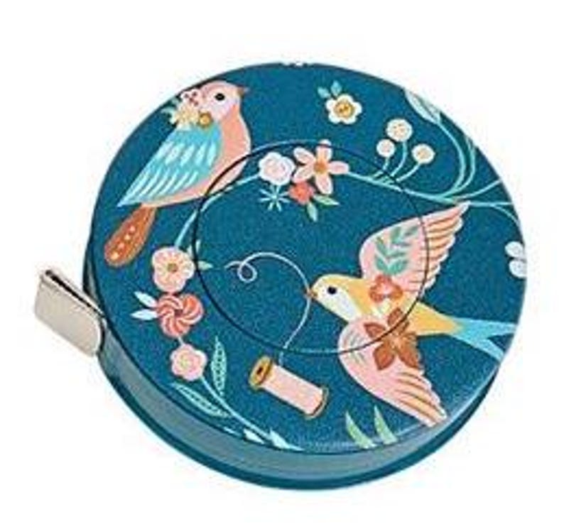 May include: A teal tape measure with a decorative bird and floral design. The tape measure features two birds, one perched and one in flight, surrounded by flowers and vines. A small metal tab is visible on the side.