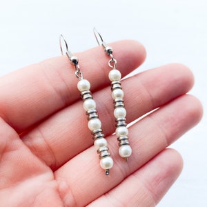 May include: A pair of silver dangle earrings with white pearl beads.
