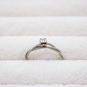 May include: A silver guitar string ring with a double-wrapped band.