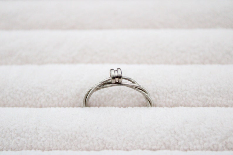 May include: A silver guitar string ring with a double-wrapped band.