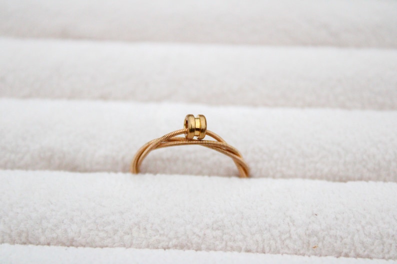May include: A gold guitar string ring with a decorative bead in the center.