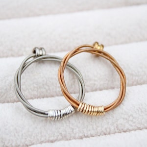 May include: Two guitar string rings, one silver and one gold, on a white background.