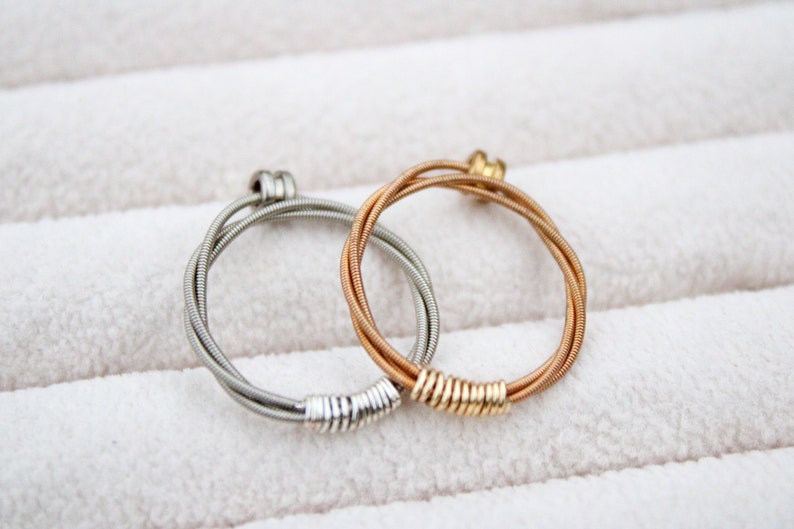May include: Two guitar string rings, one silver and one gold, on a white background.