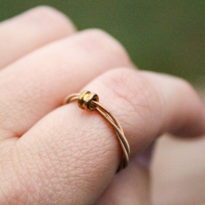 May include: A gold ring made from guitar strings with a small gold bead accent.