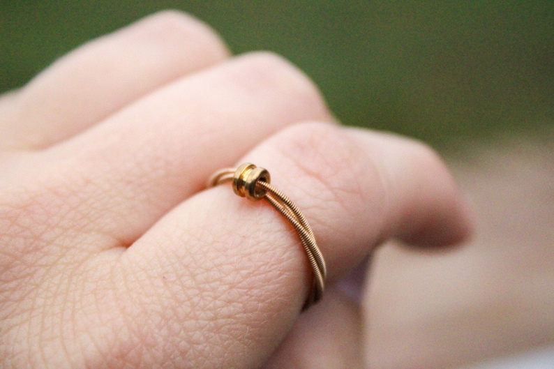 May include: A gold ring made from guitar strings with a small gold bead accent.