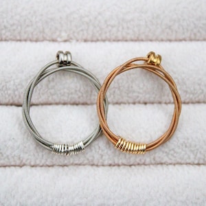May include: Two guitar string bracelets, one silver and one gold, on a white background.
