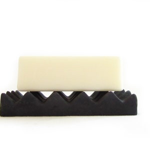 May include: A white bar of soap resting on a black, textured soap dish.
