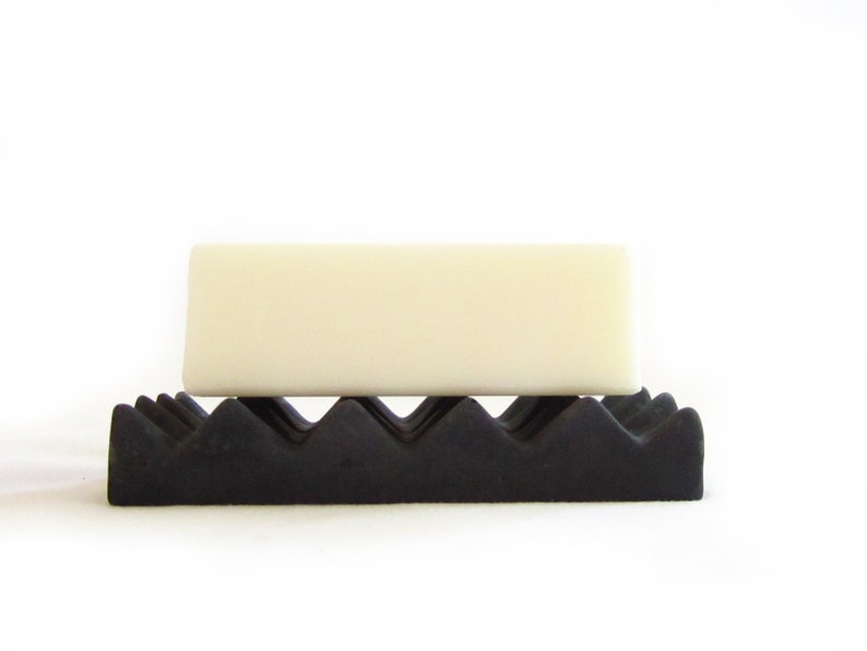May include: A white bar of soap resting on a black, textured soap dish.