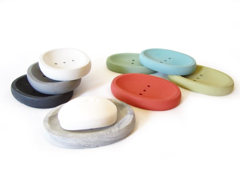Puede incluir: Un juego de seis jaboneras ovaladas en varios colores, incluyendo gris, blanco, verde, azul y rojo. Las jaboneras est&aacute;n hechas de hormig&oacute;n y tienen un acabado liso y redondeado.