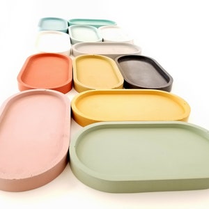 May include: A set of 12 oval-shaped concrete trays in various pastel colours, including pink, green, yellow, and grey. The trays are arranged in a staggered pattern, with the largest tray at the bottom and the smallest tray at the top.