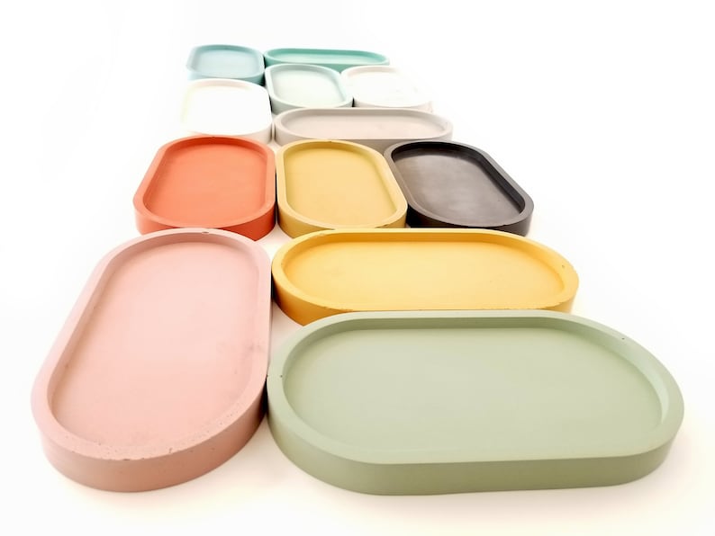 May include: A set of 12 oval-shaped concrete trays in various pastel colours, including pink, green, yellow, and grey. The trays are arranged in a staggered pattern, with the largest tray at the bottom and the smallest tray at the top.