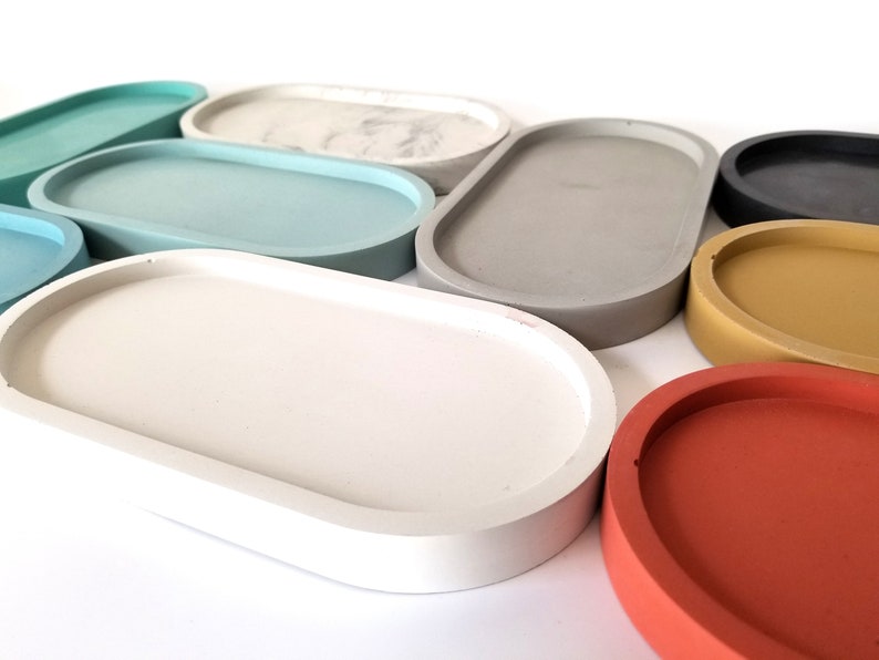 May include: A set of nine oval-shaped concrete trays in various colours, including white, grey, light blue, dark blue, yellow, and red. The trays are all the same size and shape, and they are arranged in a semi-circle.