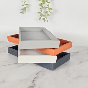 May include: Three rectangular trays stacked on top of each other. The top tray is gray, the middle tray is orange, and the bottom tray is black.