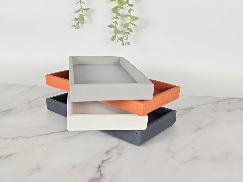 May include: Three rectangular trays stacked on top of each other. The top tray is gray, the middle tray is orange, and the bottom tray is black.
