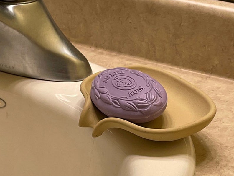 May include: A purple bar of soap with the word "Avon" embossed on it, sitting in a beige soap dish.