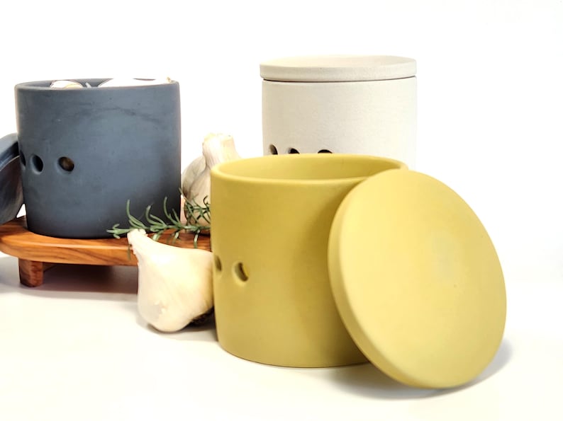 May include: Three ceramic garlic keepers with lids. One is blue, one is white, and one is yellow. The yellow keeper is open, revealing the lid.