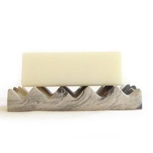 May include: A white bar of soap resting on a gray and white marble soap dish with a wavy design.