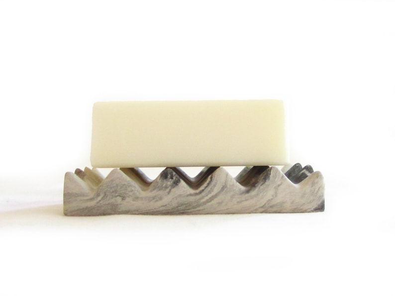 May include: A white bar of soap resting on a gray and white marble soap dish with a wavy design.
