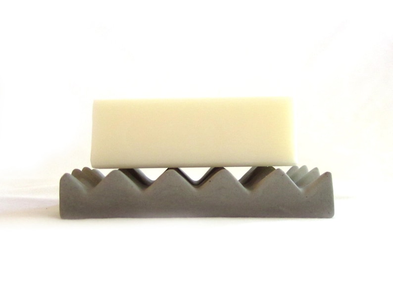 May include: A gray concrete soap dish with a wavy design, holding a white bar of soap.