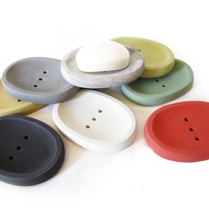 Puede incluir: Conjunto de ocho jaboneras ovaladas en varios colores, incluyendo gris, blanco, amarillo, verde y rojo. Las jaboneras est&aacute;n hechas de hormig&oacute;n y tienen tres agujeros de drenaje.