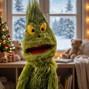 May include: A plush green character with yellow eyes and a red mouth, resembling the Grinch, is the focal point. The background includes a Christmas tree, teddy bears, and a snowy window, creating a festive holiday scene.